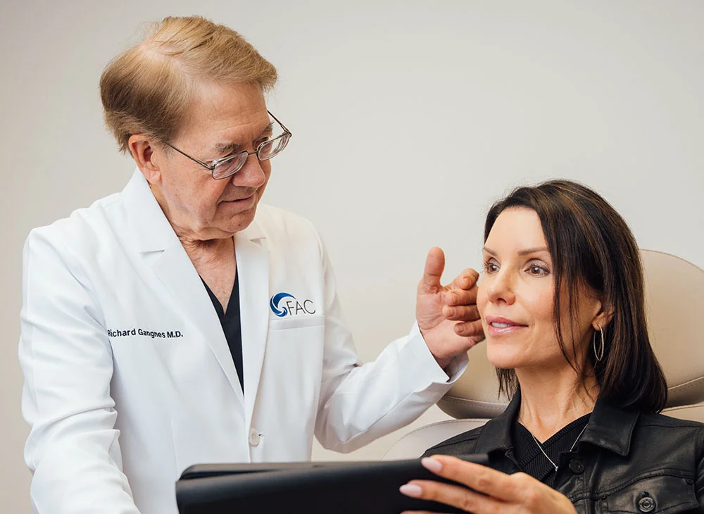 Dr. Richard Congnes, a dermatologist, examines a patient in a medical setting. The patient, wearing a leather jacket, appears attentive as Dr. Congnes gently assesses her. The image highlights the doctor-patient interaction and emphasizes personalized healthcare. - Mini Facelift in San Clamente, Aliso Viejo and Rancho Santa Margarita, CA